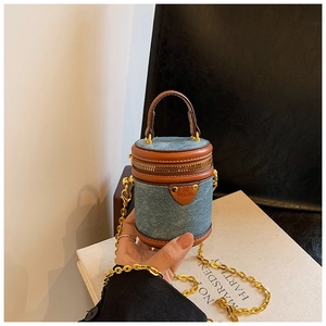 Detail einer Zylindertasche aus Denim und Leder mit Goldkette auf Kunstbüchern