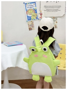 Detailed back view of a child wearing the cute green frog backpack in a cozy indoor setting