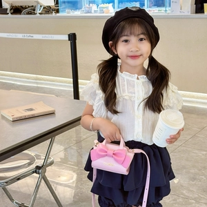 Pink kids crossbody bag with large bow and adjustable strap in a cafe setting