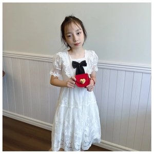 Detailed view of red heart crossbody bag with gold chain strap on girl in white dress