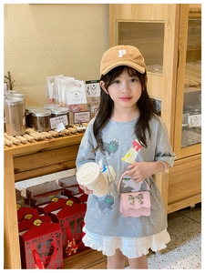Pink crossbody bag with gold bow and chain strap on child model in casual setting