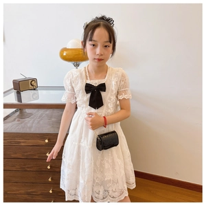 Detail of white lace dress featuring floral embroidery and black bow for girls