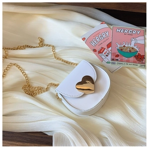 Detail of white mini heart-shaped crossbody bag with gold metal chain and heart clasp