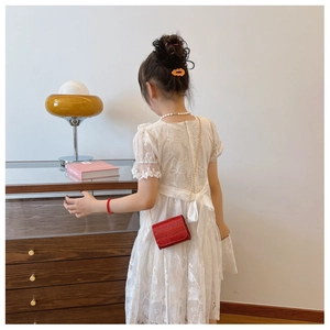 Detail view of a mini red crocodile texture crossbody bag with gold chain on lace dress
