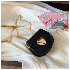 Detail of a kids' black leather crossbody bag featuring a golden heart-shaped metal clasp