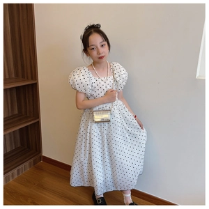 Girl wearing white polka dot puff sleeve dress with silver crocodile pattern chain bag