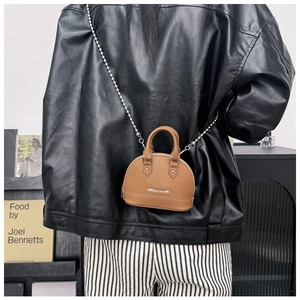 Detailed view of a tan lychee leather shell bag with silver bead chain worn by a model