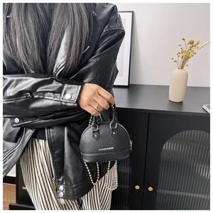 Close-up of black shell-shaped crossbody bag with chain strap and printed text detail