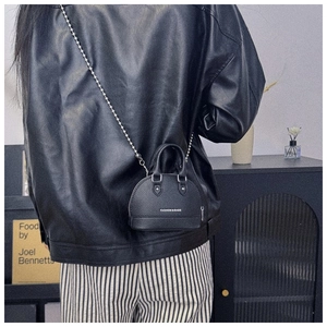 Detail of black shell-shaped shoulder bag featuring silver ball chain and leather texture