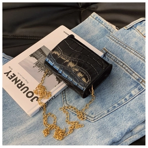 Detail of black faux leather crossbody bag with crocodile texture and gold chain strap