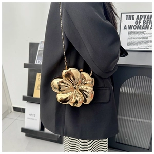 Detail of a golden flower-shaped metal clutch bag with mirror finish and elegant chain strap