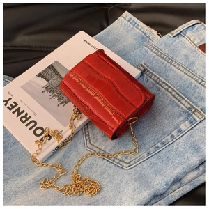 Close-up of red crocodile pattern chain bag with gold metal strap on denim