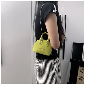 Close-up of a neon shell-shaped mini handbag with a silver chain and top handle on a model