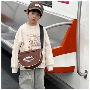 Détail d'un sac bandoulière enfant en similicuir marron avec lettres blanches dans le métro