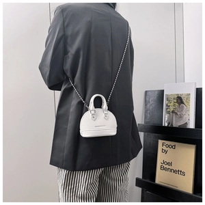 Detail of white lychee leather shell bag with elegant silver bead chain strap on model