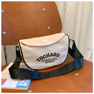 Détail du sac bandoulière beige pour enfant avec lettrage noir posé sur une chaise