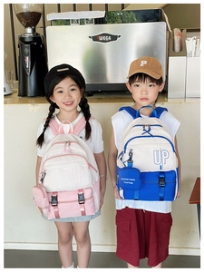 Two children wearing stylish color-block backpacks with small coin pouches in a cozy cafe