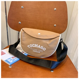 Détail du sac à bandoulière en toile kaki pour enfant avec sangle noire sur chaise en bois