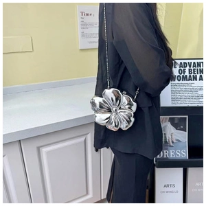 Close-up of a silver flower-shaped metallic chain bag worn by a model in a black blazer