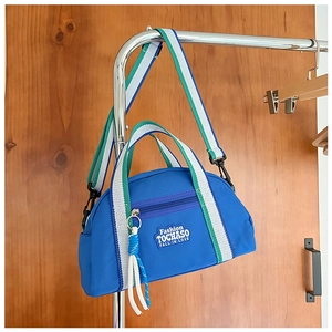 Détail du sac en toile bleue avec sangle rayée, boucle en métal et logo de mode