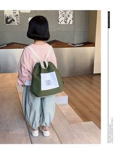 Rear view of a child wearing a grass green drawstring backpack with white rope straps