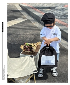 Outdoor street shot of a stylish black kids backpack with white drawstring and square pocket