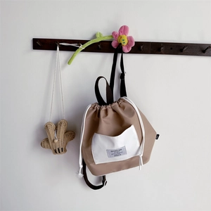Detail of khaki drawstring backpack with contrast white pocket and fabric label hanging