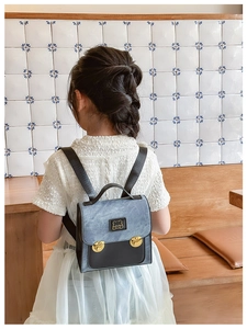 Rear view of a child wearing a blue patchwork bear backpack with gold metal buckles