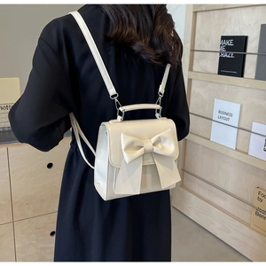 Close-up of cream white mini backpack with bow decoration on smooth faux leather surface