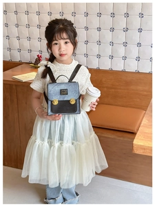 Detail of a child's bear backpack with blue fabric, black leather flap, and gold bear lock