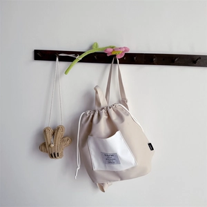 Detail of a beige drawstring backpack for kids featuring white pockets and hanging hooks