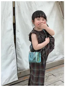 Détail d'un mini sac bandoulière brillant bleu en cuir verni pour enfant avec anse argentée