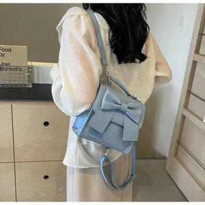 Back view of a light blue mini backpack with bow detail on a person in soft lighting