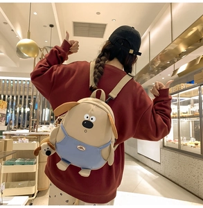 Dettaglio dello zaino a forma di cucciolo beige con salopette blu e ciondolo di peluche