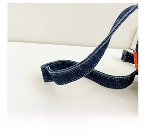 Detail showing durable denim strap with yellow stitching and orange brand label