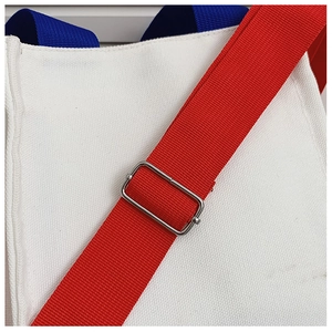 Détail de la sangle réglable rouge et boucle en métal sur un sac en toile blanc