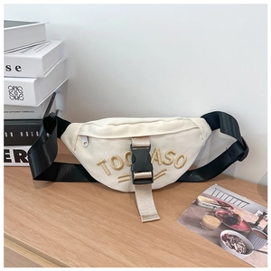 Close-up of beige canvas waist bag with 3D embroidery on a minimalist wooden table