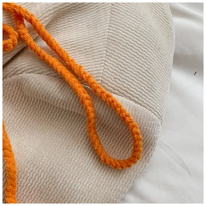 Gros plan détaillé sur la texture tricotée main et la sangle tissée orange du sac enfant