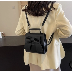 Detail of a black mini bow backpack worn with a beige blazer in a minimalist indoor setting