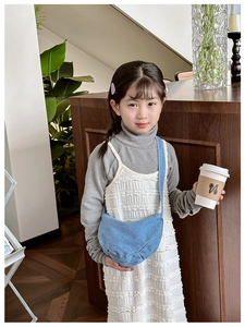 Close-up of a blue denim crossbody dumpling bag for kids on a textured white dress
