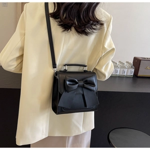 Close-up of a black crossbody bag with a large bow detail on a stylish model