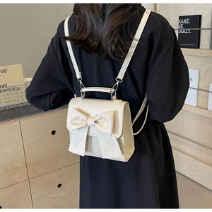 Detail of off-white mini backpack featuring a large bow and adjustable straps on a model