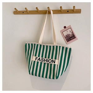 Green and white striped canvas tote bag with FASHION text hanging on a wooden hook