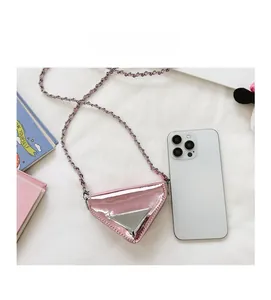 Pink triangular mini crossbody bag with metallic finish shown next to a smartphone