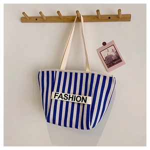Detailed view of canvas tote bag with blue vertical stripes and FASHION lettering webbing