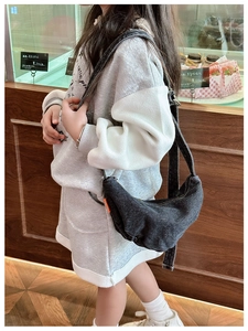 Detail of dark gray denim crescent crossbody bag with wide strap on a stylish child