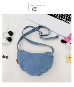 Detail of light blue denim crescent crossbody bag with adjustable strap and red label