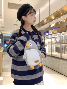 Detail einer grauen Pinguin-Plüschtasche, getragen von einem Modell in Innenräumen