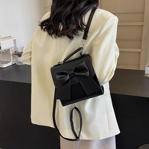 Women's black mini backpack with oversized bow detail shown worn as a crossbody bag