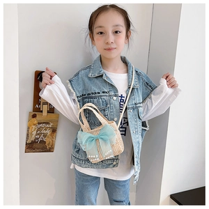 Close-up of kids straw bag with blue mesh bow and pearl charms worn by a young girl